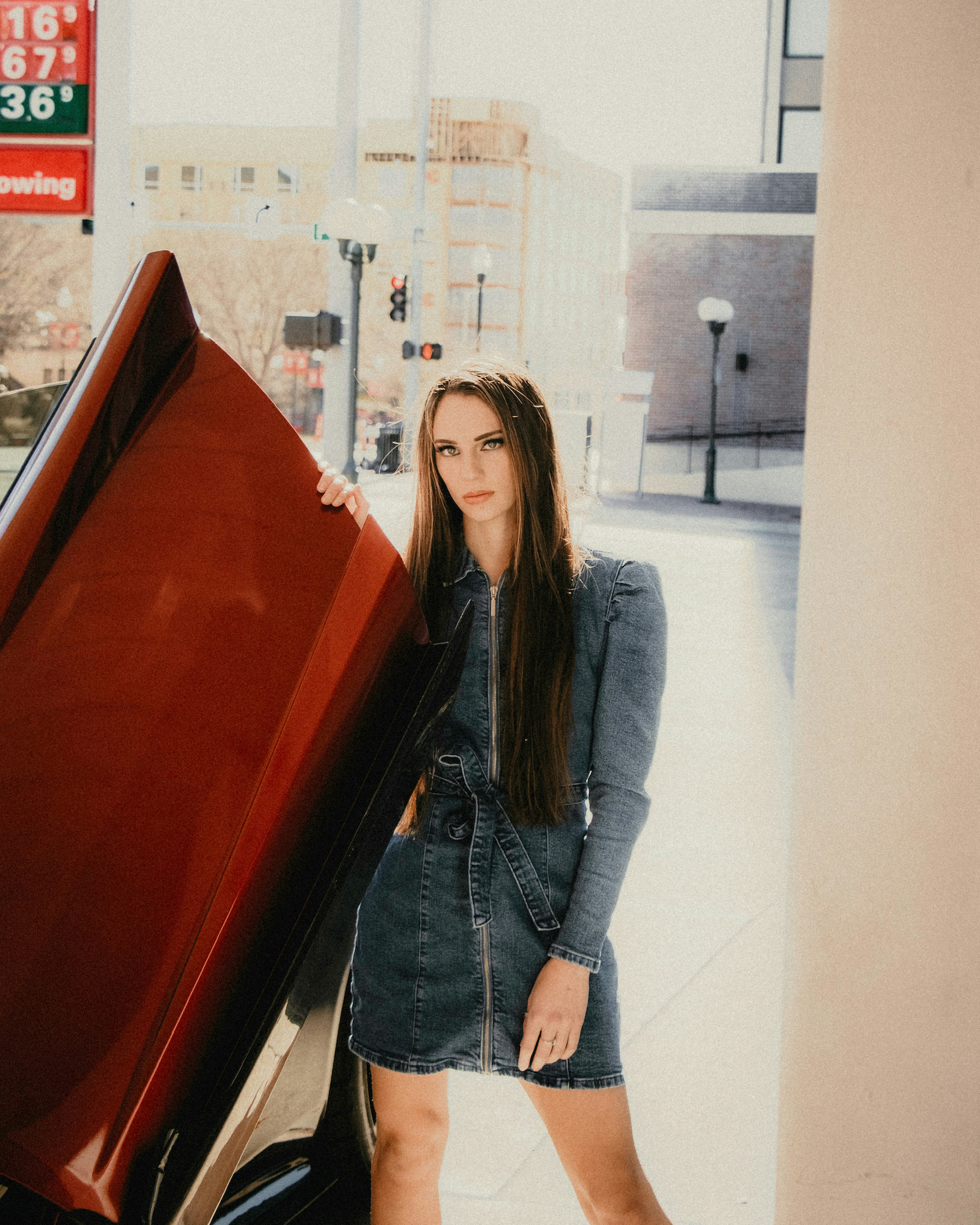 woman in blue denim jacket standing beside red car